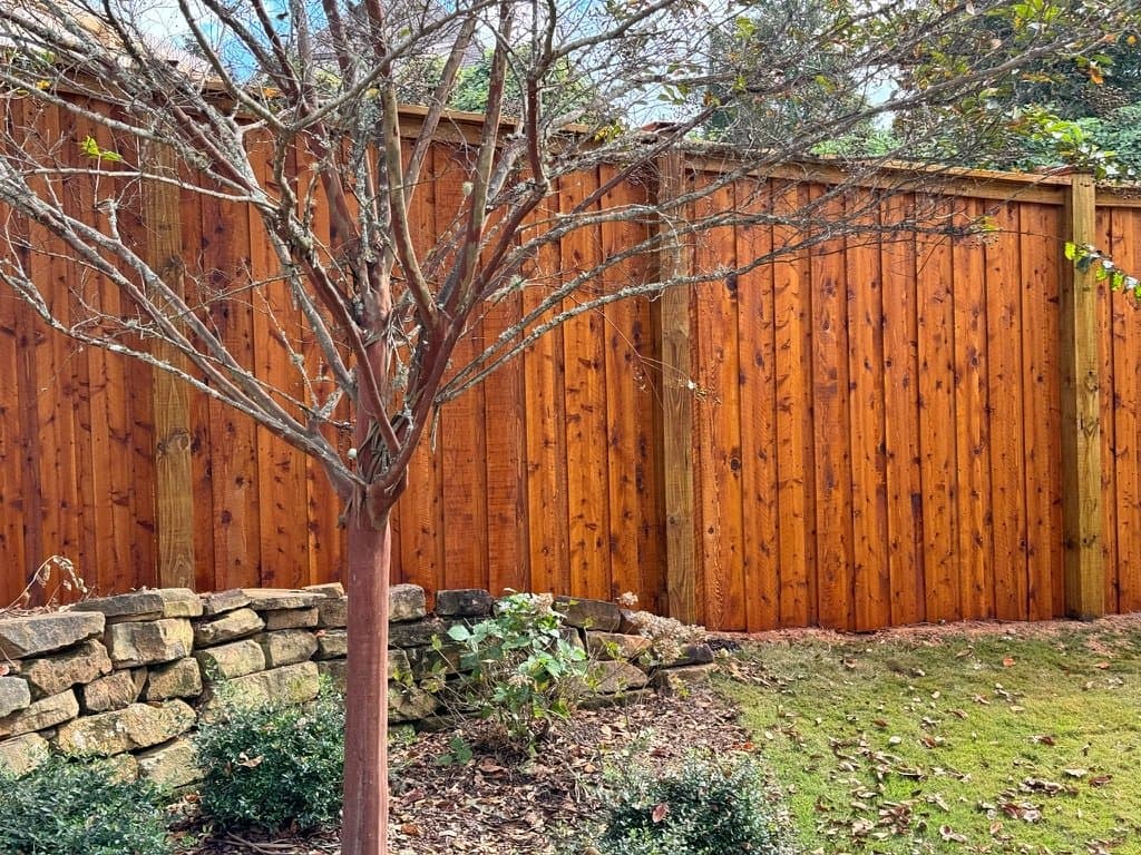 Privacy fence above a stone wall stained in Cedar